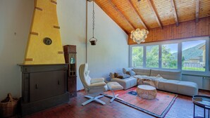 Una sala de estar con chimenea, un sofá, un sillón y vistas al exterior.