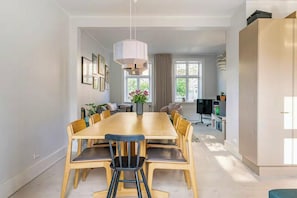 Ein moderner Essbereich mit Holztisch und -stühlen, einer Pendelleuchte sowie Blick auf die Küche und das Wohnzimmer.