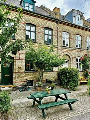 A brick building with a green door, windows, and a small garden with a picnic table.