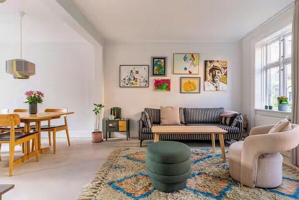 A living room with a sofa, a dining table, and a coffee table. There are framed artworks on the wall.