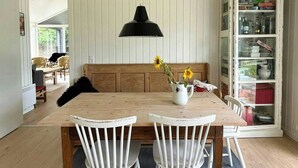 A dining area with a wooden table, white chairs, a black pendant lamp, and a cabinet with glass doors. - Idyllic view to the fjord from home (Jægerspris)