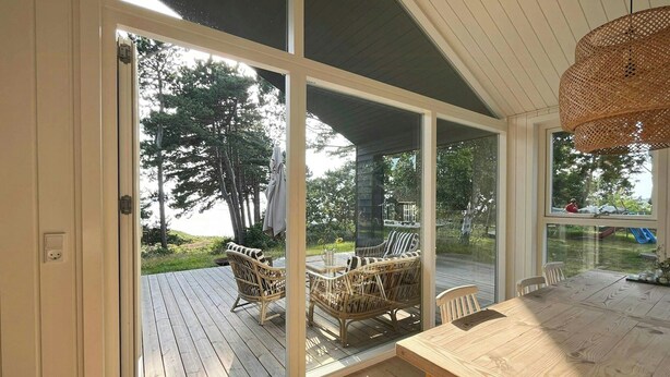 A wooden deck with wicker furniture and a glass door leading outside. - Idyllic view to the fjord from home (Jægerspris)