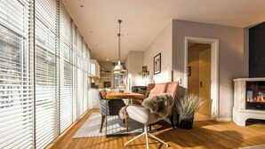 Un salon moderne comprenant un coin repas, un plancher en bois, une cheminée et de grandes fenêtres équipées de stores.