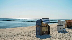 Des chaises de plage sont empilées sur le sable, près de l’eau.