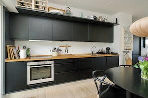 Eine moderne Küche mit dunklen Schränken, einer Holz Arbeitsplatte, einem eingebauten Backofen und einem Essbereich mit Tisch und Stühlen.