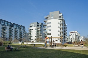 Ein Wohngebäude mit mehreren Balkonen, einem Spielplatz und einem Parkbereich mit Bänken.
