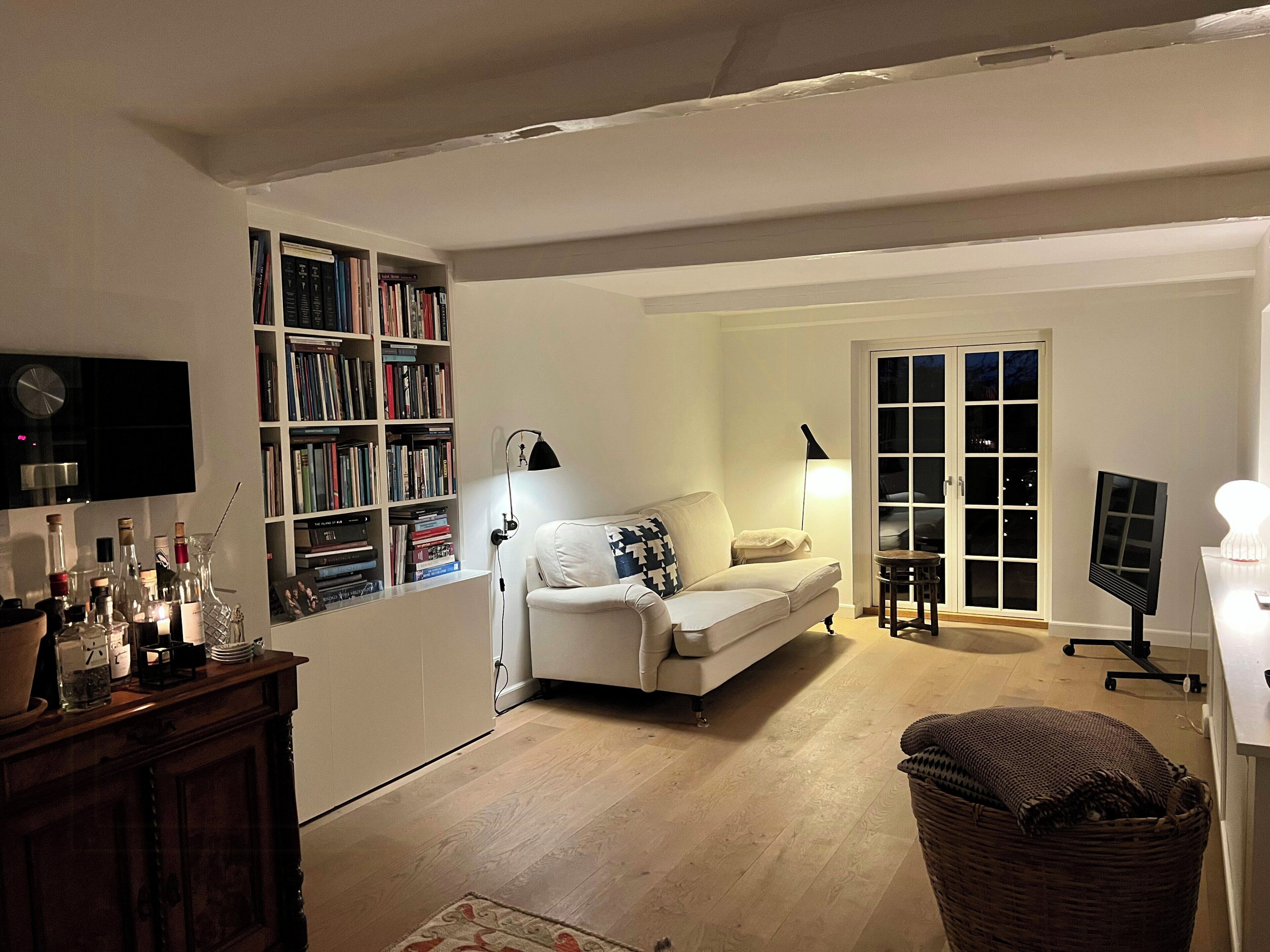 Een woonkamer met een bank, een boekenkast, een televisietoestel en een raam.
