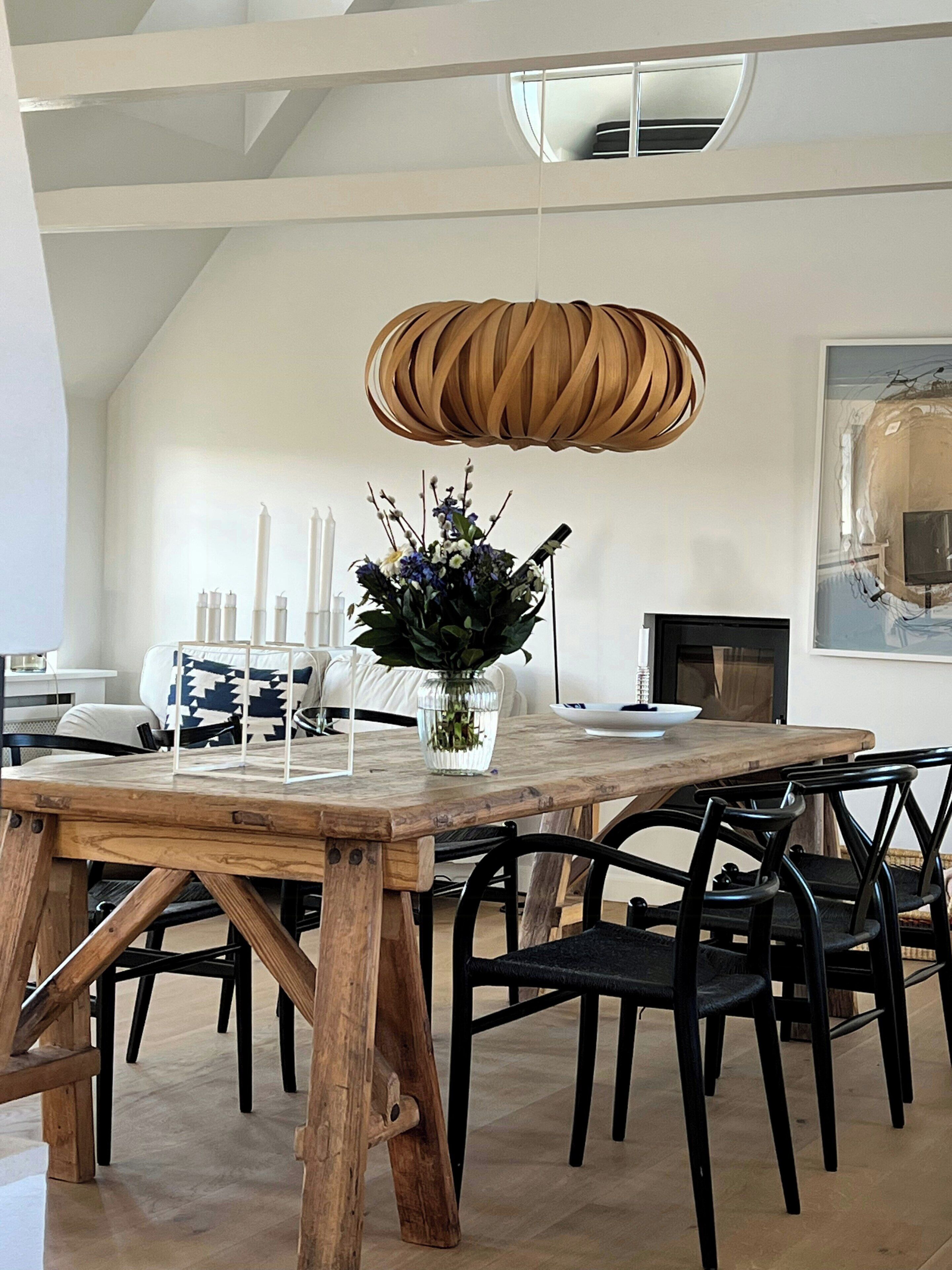 A dining area with a wooden table, black chairs, a vase with flowers, and a modern pendant light.