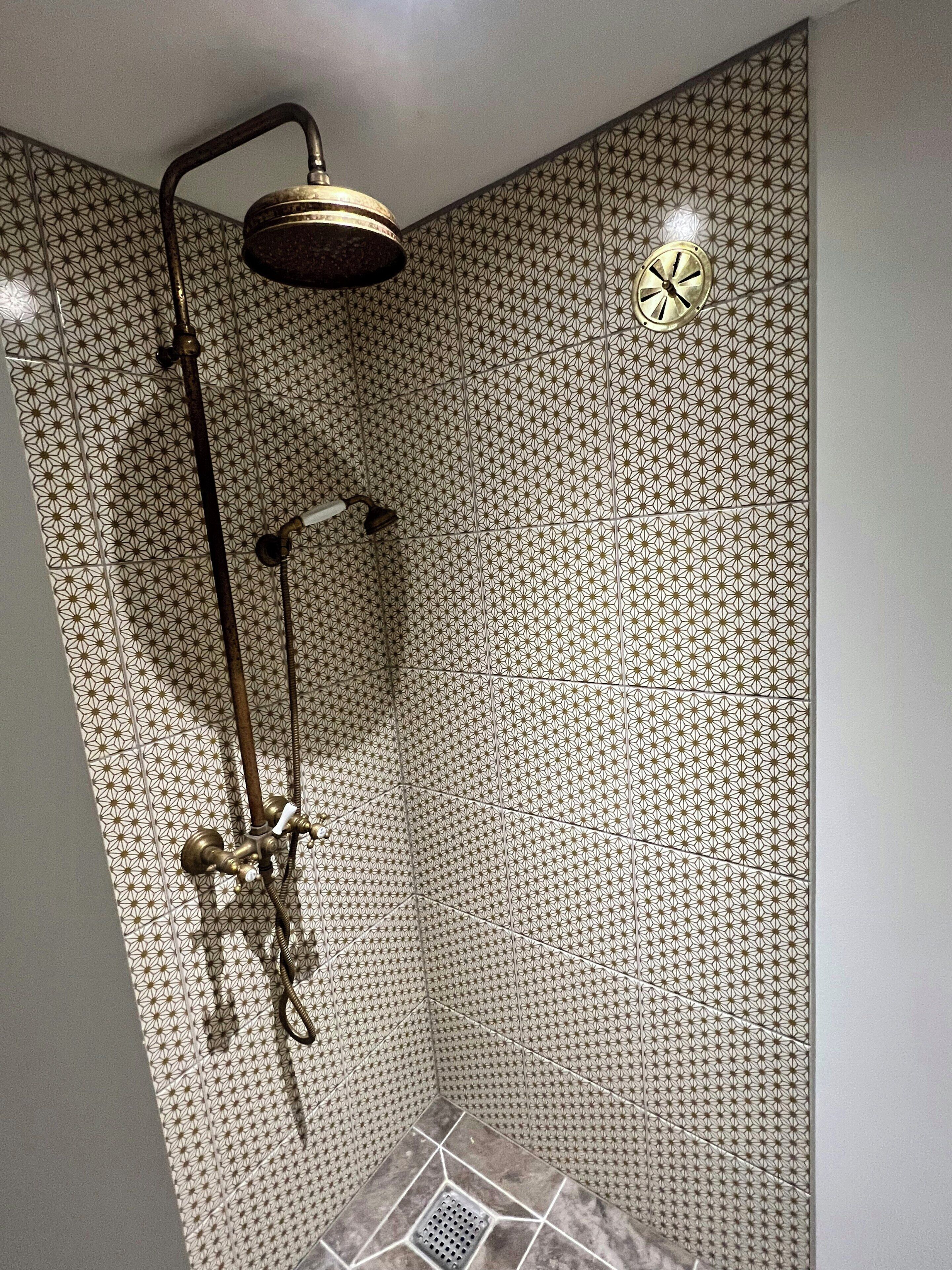 A shower with a geometric tile pattern, a handheld showerhead, and a wall-mounted clock.