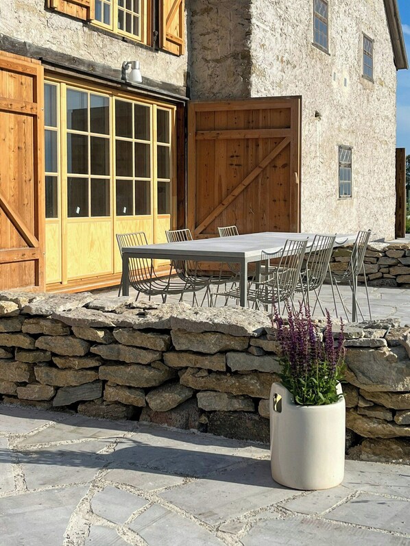A stone building with a large wooden door, a stone wall, and a table with chairs outside.