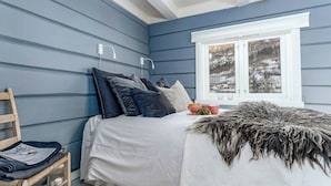 Un dormitorio con cama, almohadas, una ventana y vistas a un paisaje nevado.
