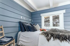 Ein Schlafzimmer mit Bett, Kissen, einem Fenster und Blick auf eine verschneite Landschaft.