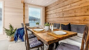 Una mesa de madera con sillas, vista de un paisaje nevado a través de una ventana y una planta en el suelo.