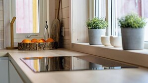 Una cocina con mostrador de madera, una cuchara de madera, un bol de naranjas y dos plantas en macetas en el alféizar.