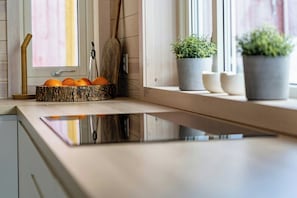 Eine Küche mit Holzarbeitsplatte, einem Holzlöffel, einer Schüssel mit Orangen und zwei Blumentöpfen auf der Fensterbank.
