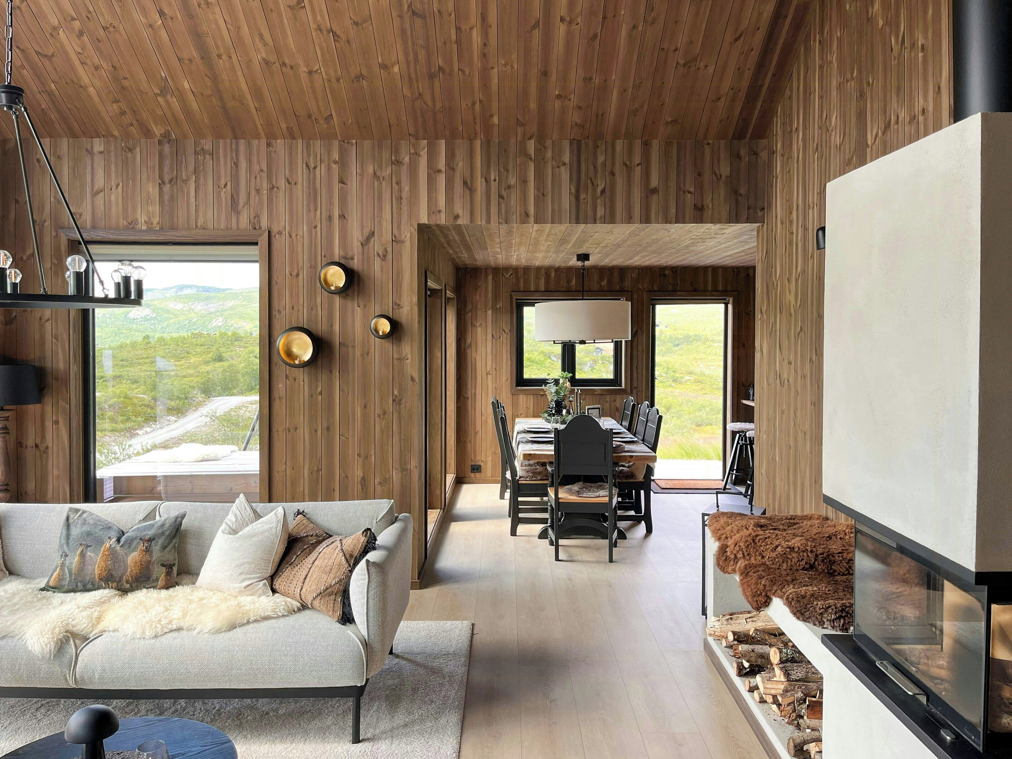 A modern interior with a wooden ceiling, a dining area with a table and chairs, and a sofa with cushions.