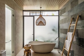 Ein modernes Badezimmer mit einer freistehenden Badewanne, einer Holzleiter und einer gewobenen Leuchte.