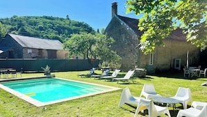 Ein Schwimmbecken mit Liegestühlen und einem Tisch, umgeben von einer Rasenfläche und Steinbauten.
