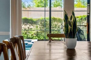Ein Holztisch mit einem Blumentopf, einem Stuhl und Blick ins Grüne durch ein Fenster.