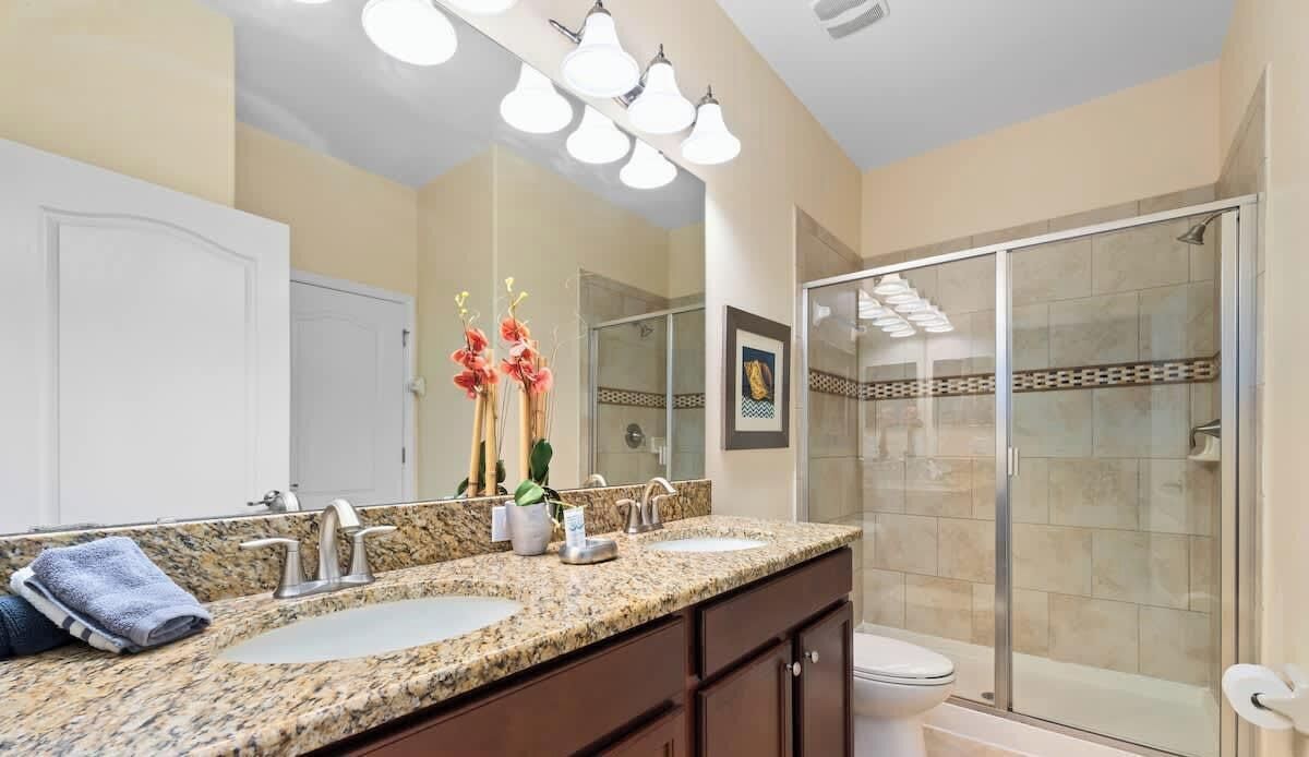 Une salle de bain avec un meuble-lavabo à deux vasques, une douche à parois de verre et des toilettes.