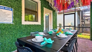 An outdoor dining area with a table set for four, surrounded by chairs, and a sign with pool rules. - 9BR Themed Close to Disney World! Movie Theatre! (Four Corners)