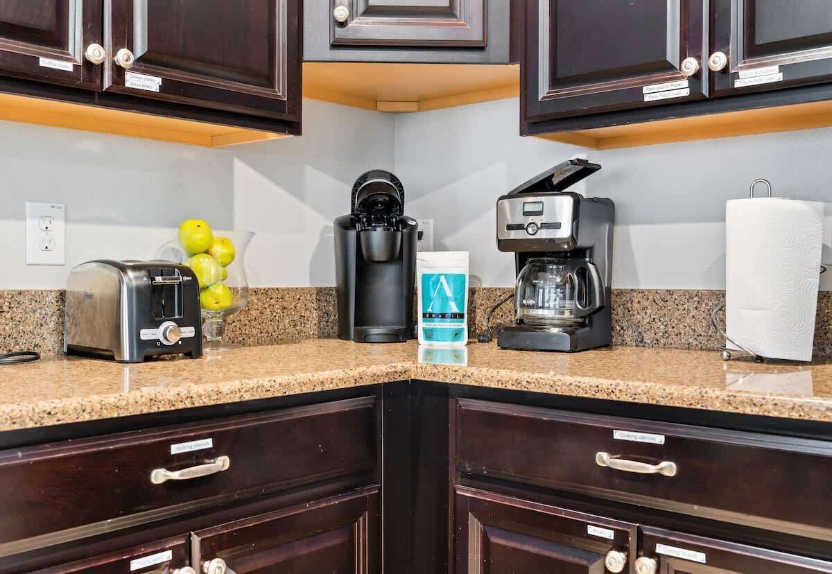 Una cucina con mobili impiallacciati in legno scuro, un piano di lavoro in granito, una macchina da caffè, un tostapane e un sacchetto di caffè.