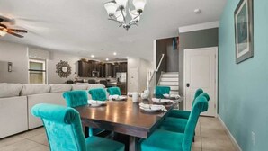 A dining area with teal chairs and a wooden table, a kitchen in the background, and a staircase leading to another level. - 9BR Themed Close to Disney World! Movie Theatre! (Four Corners)