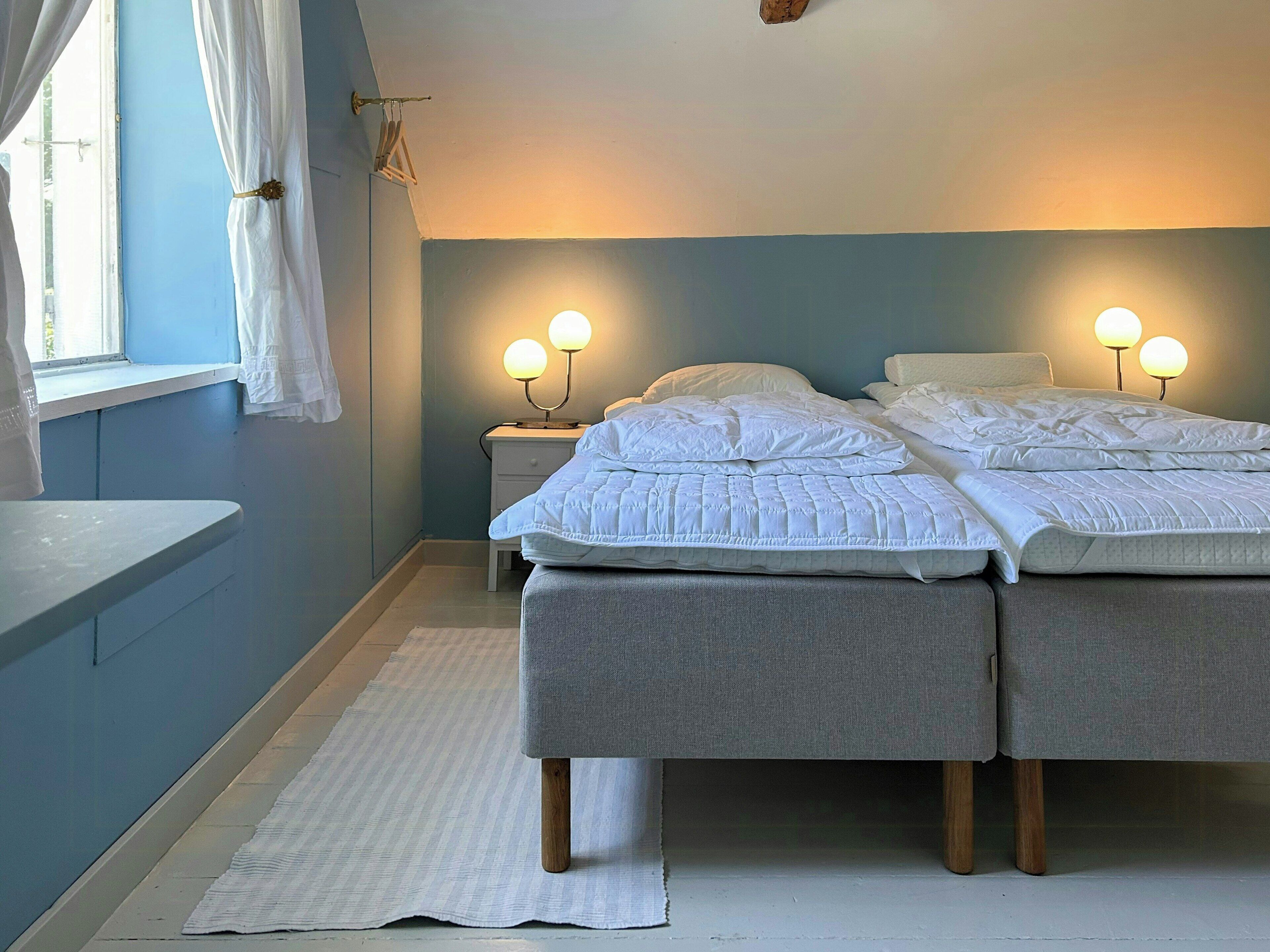 Un dormitorio con dos camas, una mesita de noche y un ventanal con cortinas.