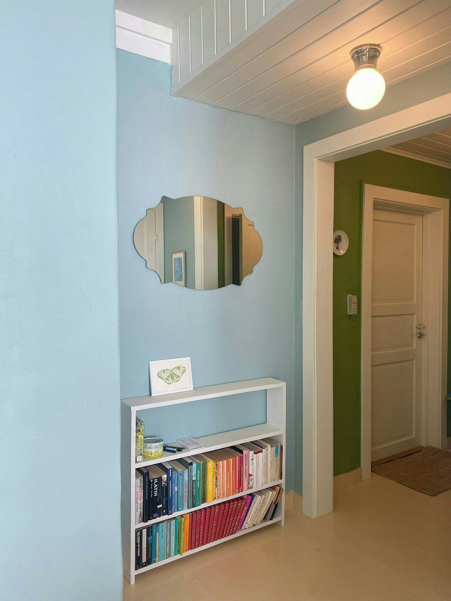 Un corridoio con una libreria, uno specchio e una porta.