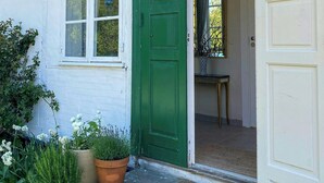 Um edifício branco com porta verde, janela e plantas em vasos.