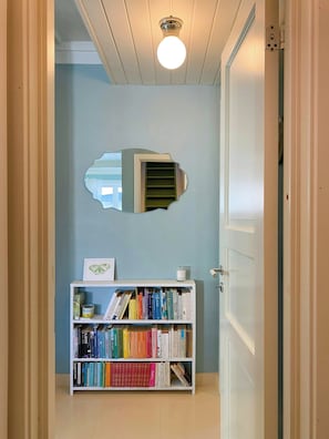 A hallway with a white door, a bookshelf with books, a framed picture, and a ceiling light fixture.