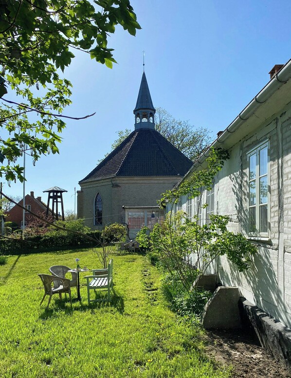 A church with a steeple, a garden with chairs, and a building with windows.