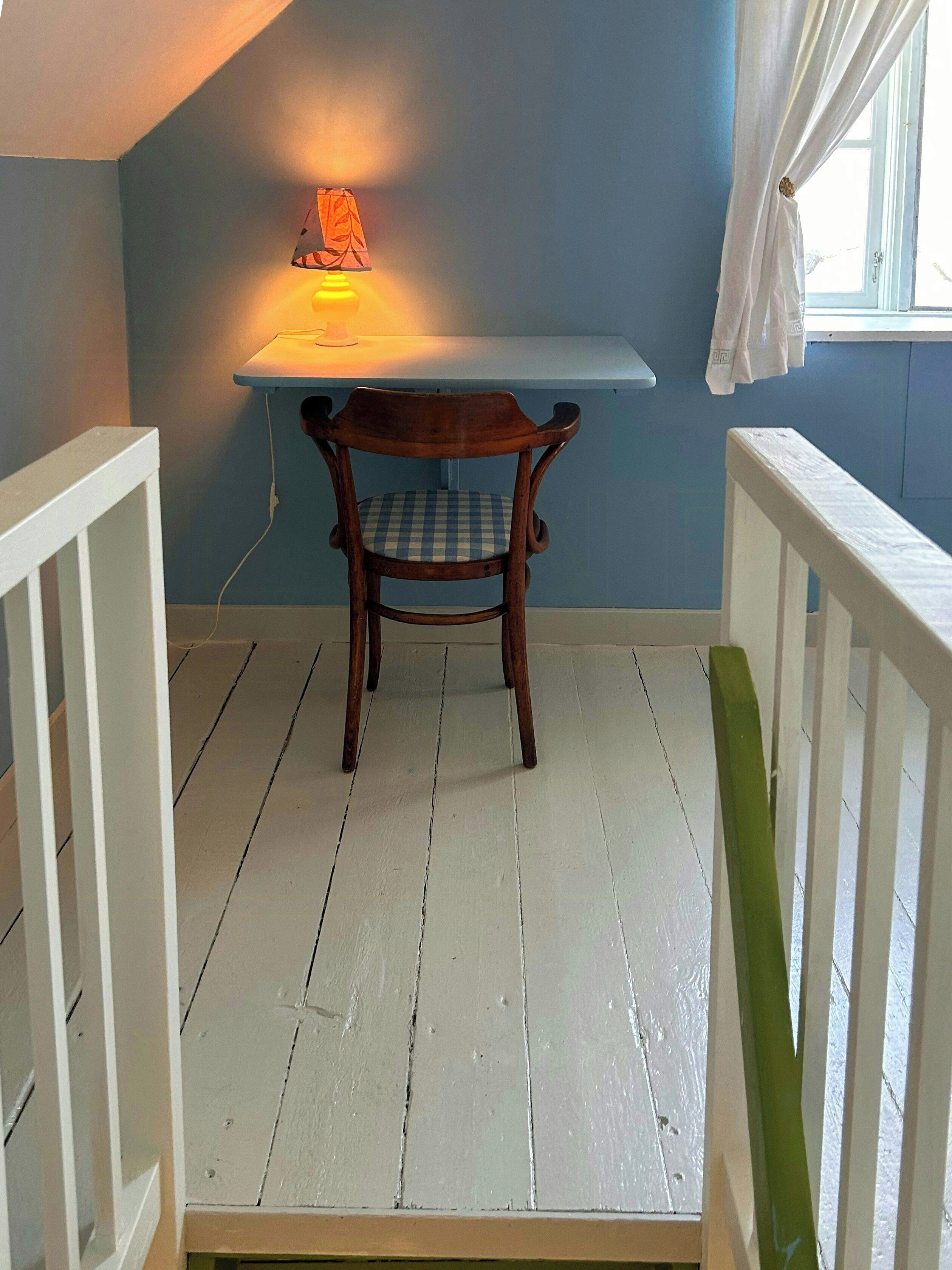 A room with a wooden chair, a white table, and a window with curtains.