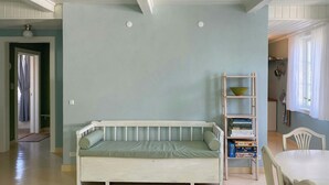 Um quarto com sofá branco, estante de livros, mesa de jantar e cozinha ao fundo.