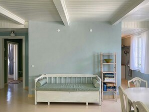 Una habitación con sofá blanco, estantería, mesa de comedor y zona de cocina al fondo.