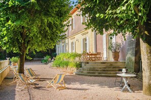 Ein Innenhof mit Sitzgelegenheiten im Freien, ein Gebäude mit Ziegeldach und ein großer Baum, der Schatten spendet.