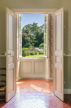 Ein offenes Jalousie mit Blick auf einen Garten und Bäume.