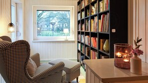 Un coin lecture confortable avec un fauteuil à motif pied-de-poule, une bibliothèque remplie de livres et une fenêtre donnant sur les arbres.