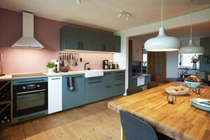 A modern kitchen with grey cabinets, a wooden dining table, and hanging pendant lights. - Holiday home with garden and sauna in Mecklenburg (Hohen Demzim)