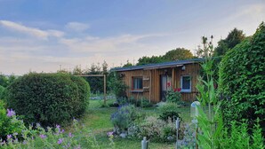 Une cabane en bois avec un jardin devant, entourée d’un feuillage dense.