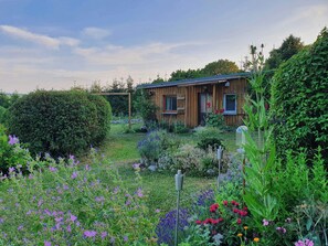 Een houten hutje met een tuin ervoor, omringd door weelderige begroeiing.