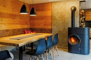 Un interior moderno con una mesa de comedor de madera, sillas azules, luces colgantes y un estufa de leña.