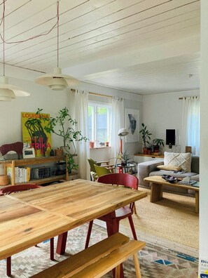 A living room with a wooden table, red chairs, a sofa, and a bookshelf. - Cosy house surrounded by nature (Diö)