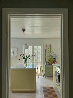 A kitchen with a central island, wooden flooring, a hanging light fixture, and a window with a view. - Cosy house surrounded by nature (Diö)