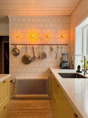 A kitchen with white subway tiles, a hanging pot rack, a built-in stove, and a window. - Cosy house surrounded by nature (Diö)