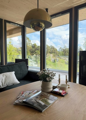 Ein Zimmer mit großem Fenster, einer Couch, einem Tisch mit Zeitschrift, einer Blumenvase und einem Kerzenständer.
