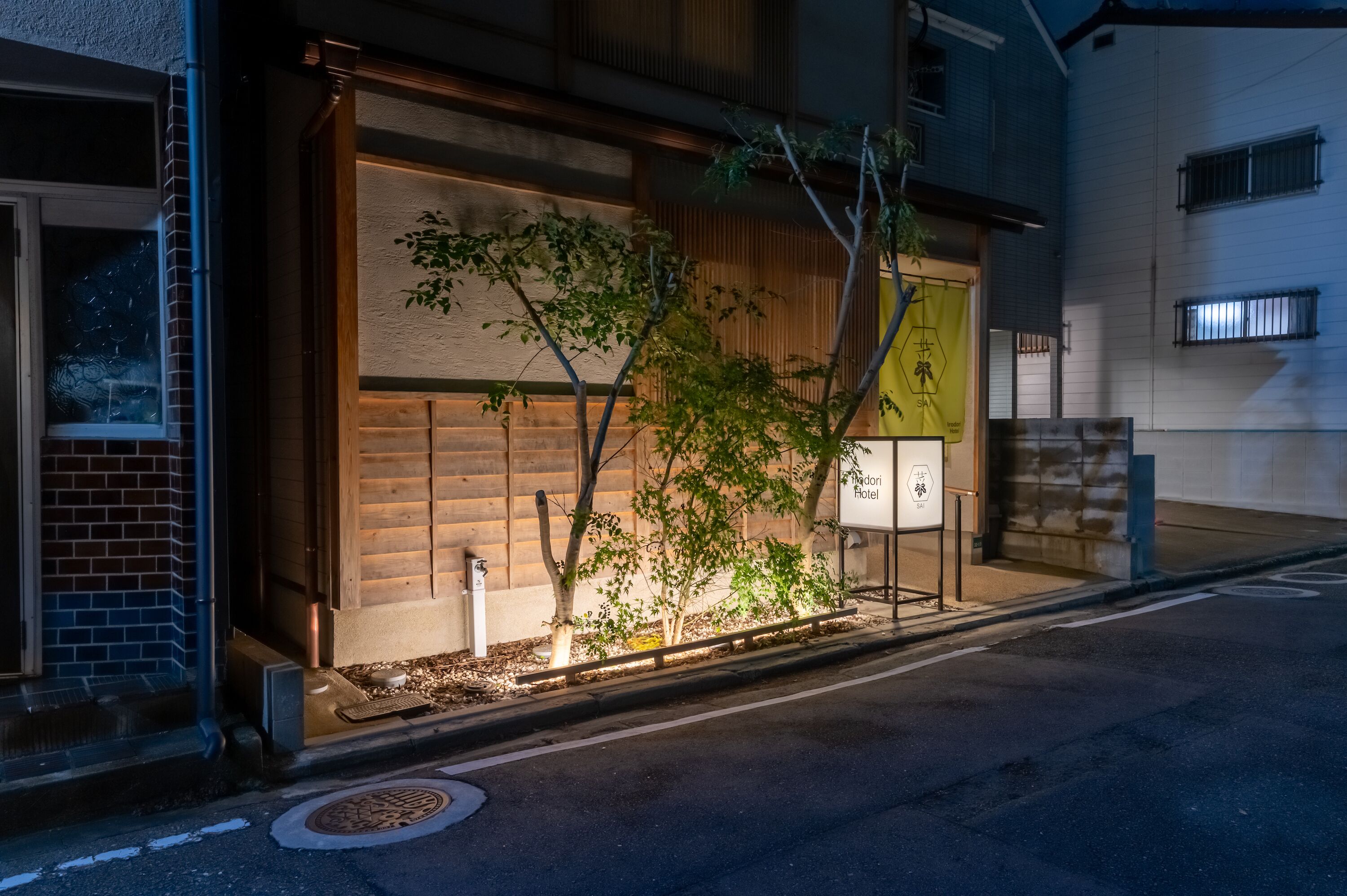 A hotel entrance with a wooden facade, a small tree, and a signboard.