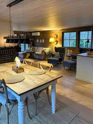 Ein gemütliches Wohnzimmer mit Kamin, einem Esstisch mit Platzsets und einer Küchenzeile mit Blick ins Freie.