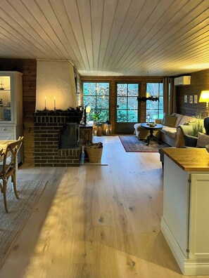 Ein gemütliches Wohnzimmer mit Kamin, Holzböden, einem Essbereich und großen Fenstern.