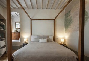 A bedroom with a four-poster bed, bedside lamps, a wooden headboard, a bookshelf, and a window with a view. - Historic apartment with terrace in Suvereto (Suvereto)